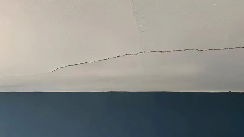 A crack running along the seam where a painted ceiling meets the wall, the paint split and lifted along its length, above a deep blue painted wall