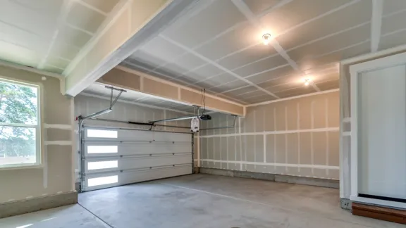 Garage interior with the walls and ceiling drywalled and taped, overhead door closed and a door through to the house
