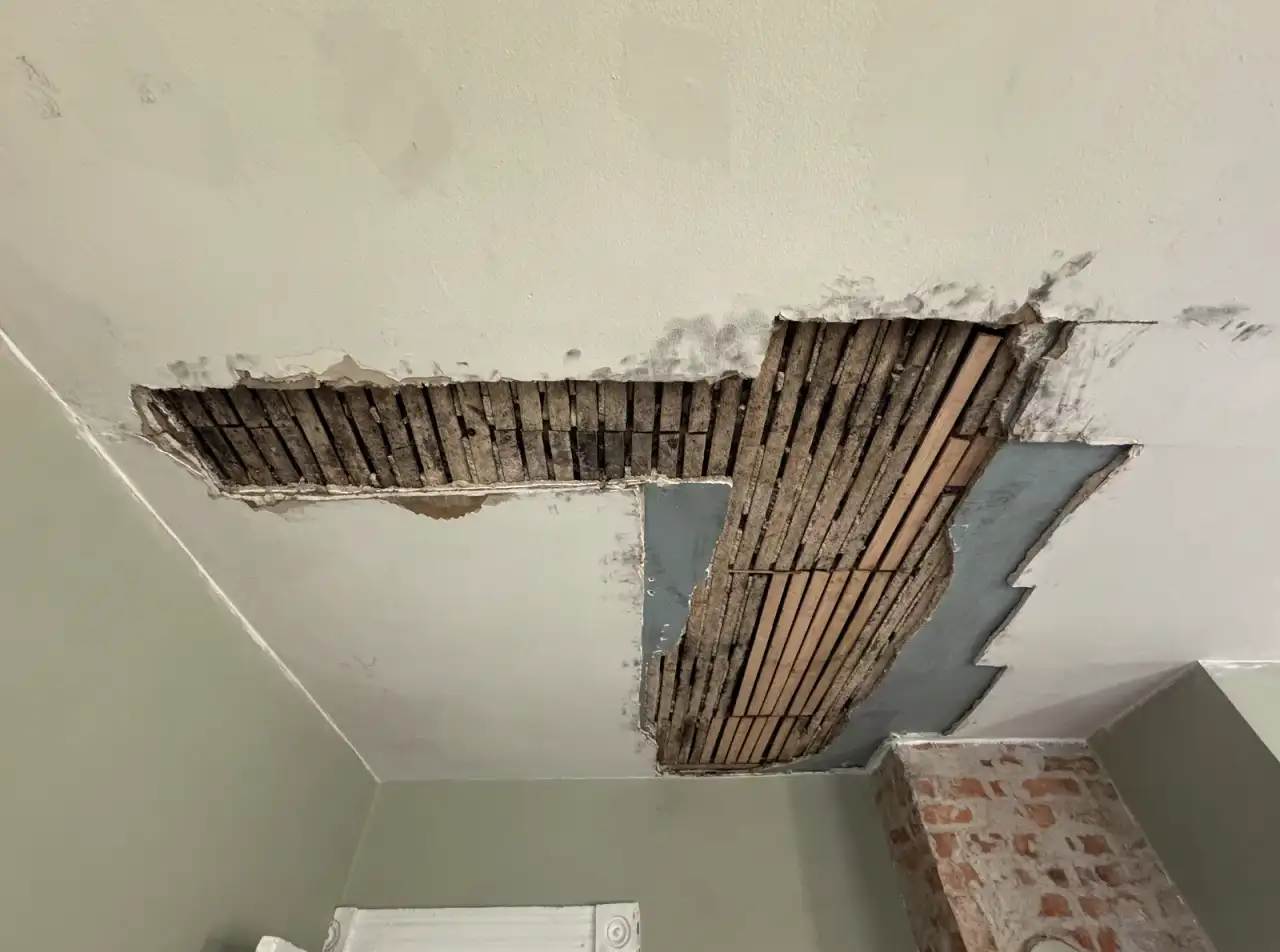 Ceiling plaster collapsed in two areas exposing wood lath, with an old brick chimney breast alongside